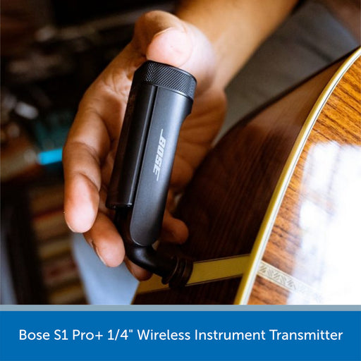 Hand holding a Bose S1 Pro+ wireless instrument transmitter with an acoustic guitar in the background.