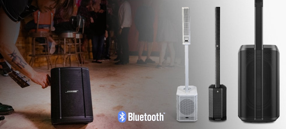 Bose speakers with Bluetooth logo on a blurred background of people and chairs.